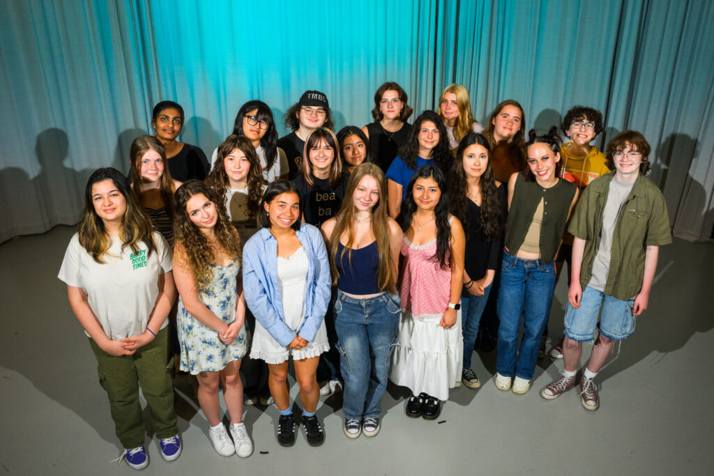 A group of 19 young people pose for a photo in a studio